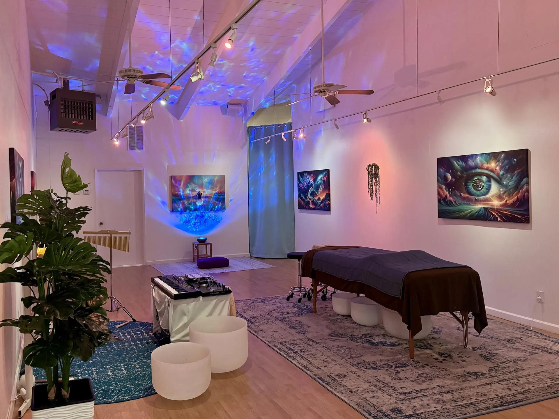 The Cotati studio in the evening: soft blue and violet light moving across the vaulted ceiling above the table, crystal singing bowls and a tall plant.