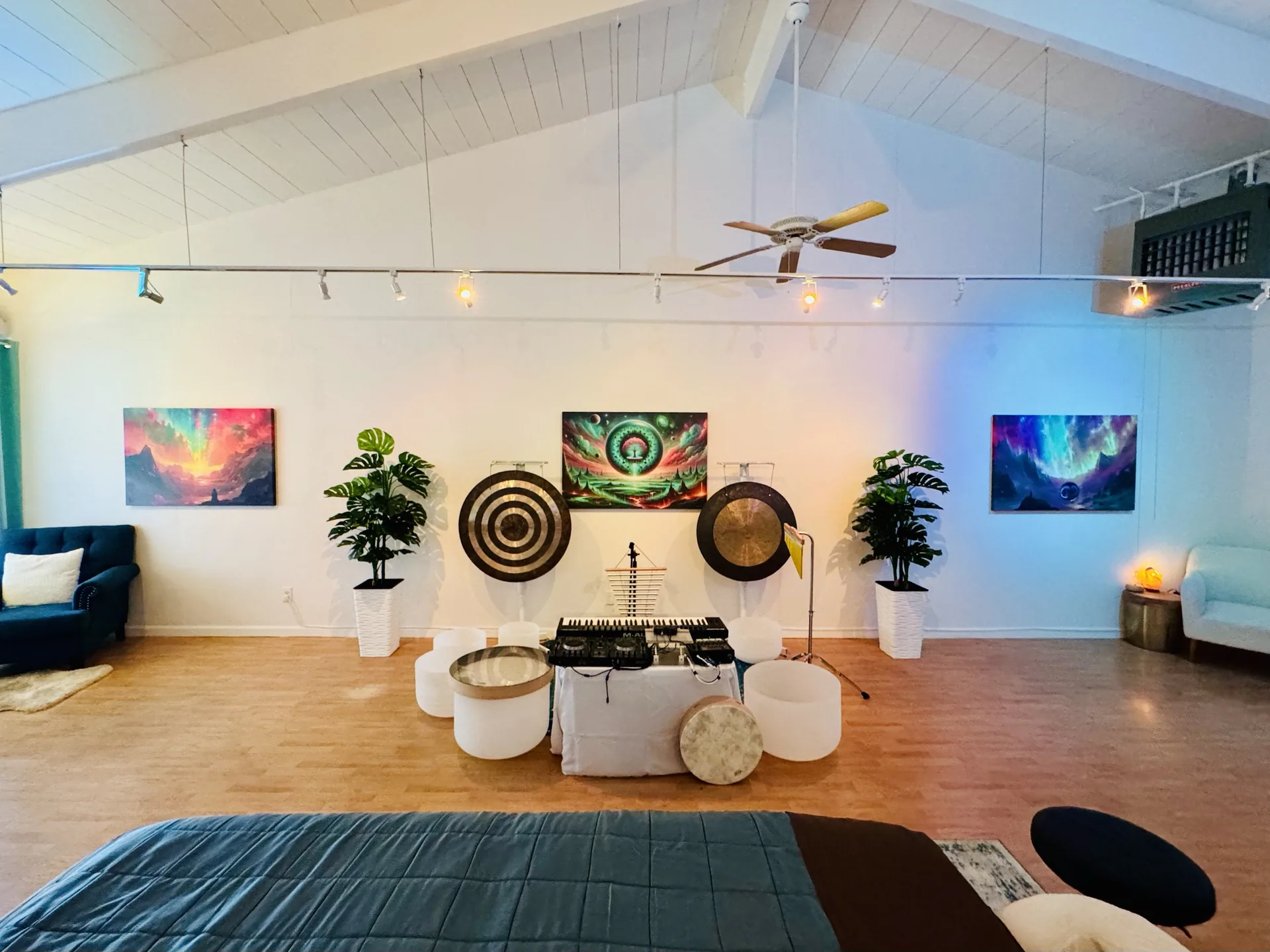 The Cotati studio in daylight: a vaulted, beamed ceiling over a wood floor, large paintings on the walls, two gongs and crystal singing bowls at the far wall, and a table in the foreground.