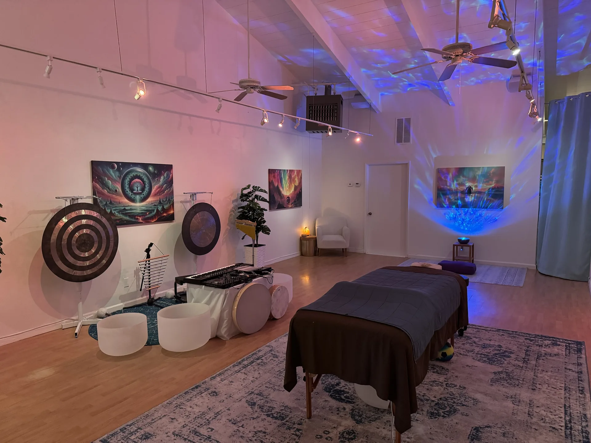 The Cotati studio in soft evening light, with gongs, crystal singing bowls and plants along the far wall, a white armchair, and the table in the foreground.